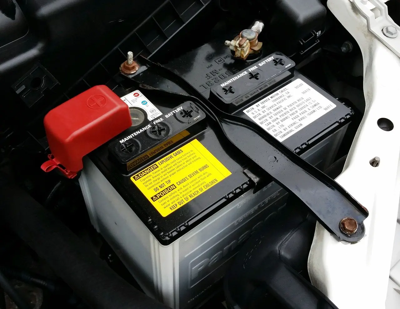 Car battery with covered positive terminal in an engine bay